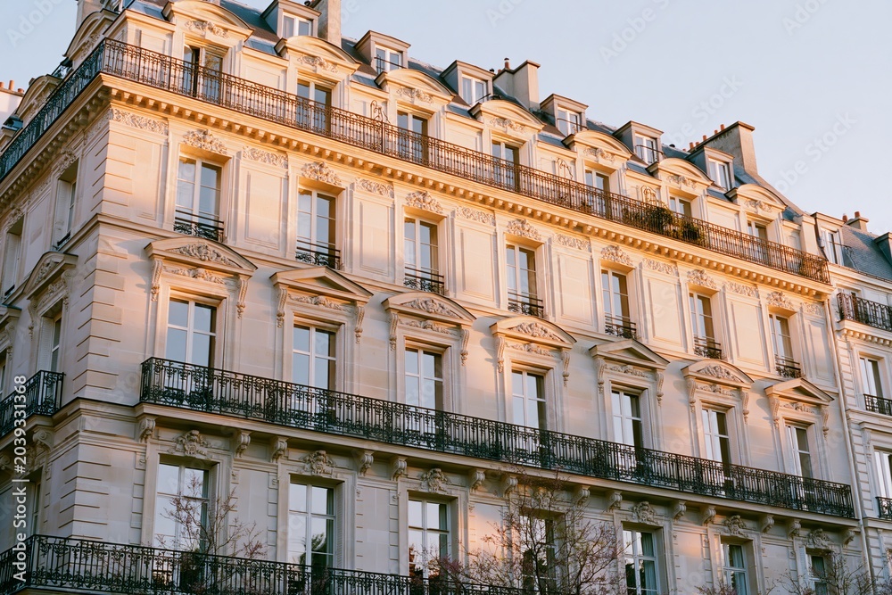 Fototapeta premium Refined Parisian mansion facade featuring intricate architectural details, warm ivory tones, and elegant balconies under soft evening light in a historic urban setting
