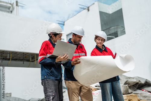 Female construction professionals discussing project updates outside unfinished building. Engineering teamwork. Developer team standing outside unfinish property with blueprint.