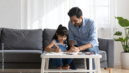Father and young daughter drawing together in living room.