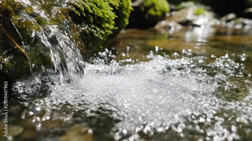 Spring water flows over mossy rocks in a pristine mountain stream creating clear bubbles and refreshing ripples.
