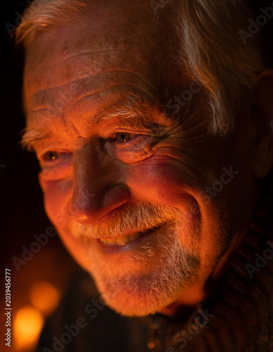 Smiling senior elderly man with beard looking away by warm orange firelight