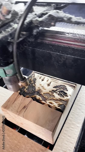 A CNC laser machine burns out a relief landscape on a wooden block