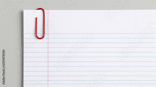 A single bright red metallic paper clip is securely attached to the top corner of a clean white sheet of lined notebook paper for organization.