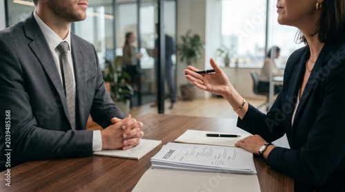 Corporate hr manager interviewing male job applicant at desk with resume in modern office background