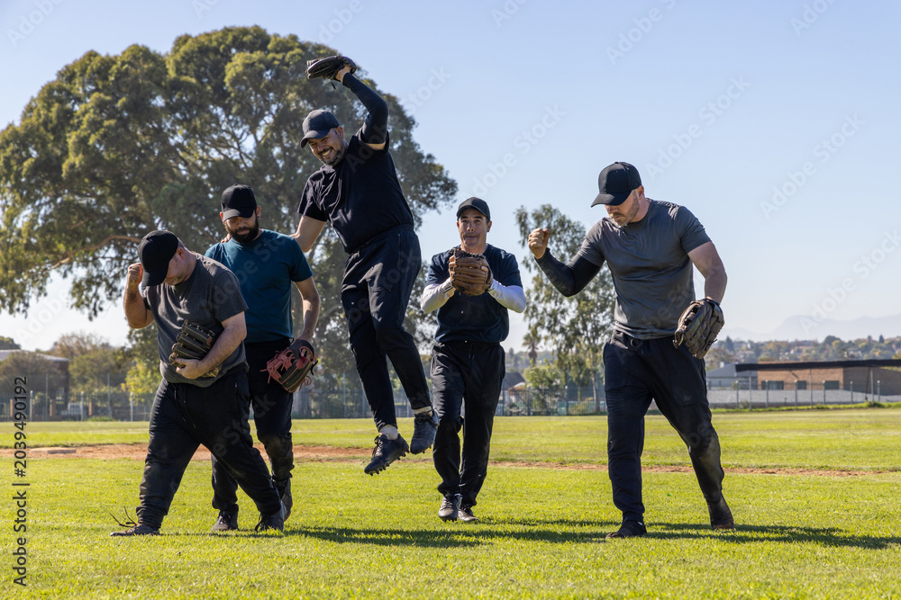 Obraz premium Diverse male teammates in athletic wear and caps walking and leaping across outfield with gloves