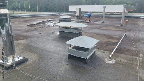 Workers maintain ventilation units on a commercial roof during a sunny afternoon in a suburban area