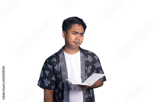 Bild auf Leinwand Indonesian man holding an open notebook with a cynical, doubtful, or displeased facial expression
