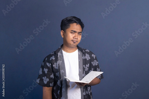 Fotografía Indonesian man holding an open notebook with a cynical, doubtful, or displeased