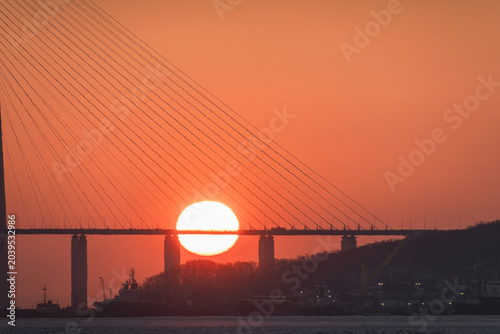 Bild auf Leinwand Sunset view behind a suspension bridge with cables silhouetted against an orange
