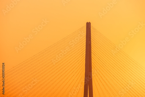 Bild auf Leinwand Suspension bridge tower with cables silhouetted against a vibrant orange sunset