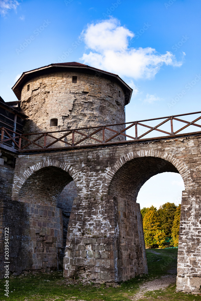Fototapeta premium A stone archway supports a wooden walkway leading to a round, stone tower. The tower is part of the Koporje fortress on a summer day with blue skies.