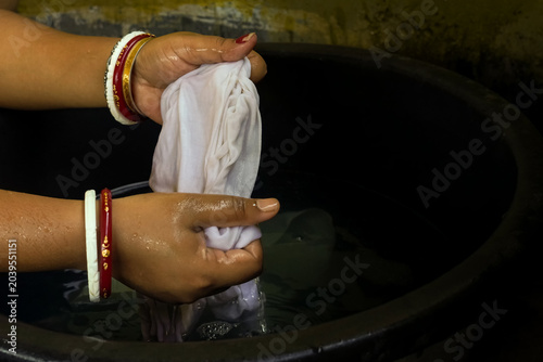A woman hand washing clothes in a black plastic basin with water, representing traditional laundry, household chores and rural lifestyle, concept of hygiene and daily life.