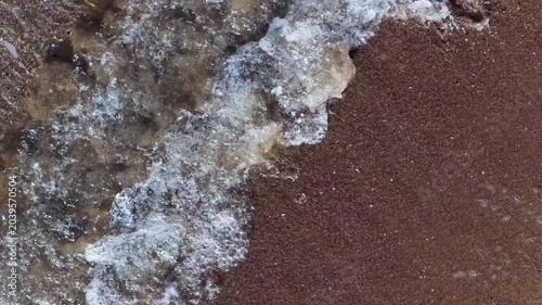 Il bagnasciuga della spiaggia col mare calmo e cristallino.
Vista dall'alto delle onde sulla sabbia della spiaggia. Ripresa in 4K
