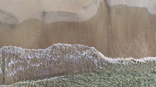 Il bagnasciuga della spiaggia col mare calmo e cristallino.
Vista dall'alto delle onde sulla sabbia della spiaggia. Ripresa in 4K
