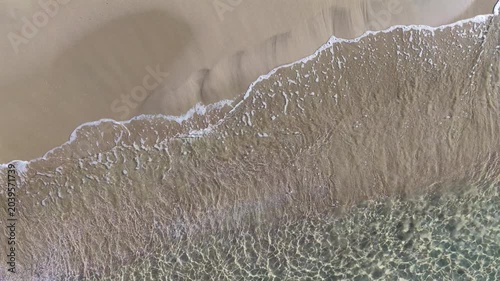 Il bagnasciuga della spiaggia col mare calmo e cristallino.
Vista dall'alto delle onde sulla sabbia della spiaggia. Ripresa in 4K
