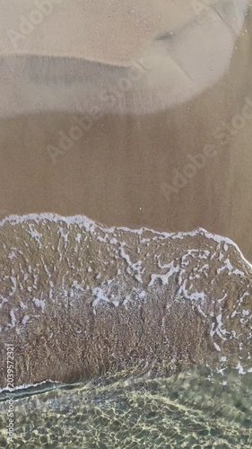 Il bagnasciuga della spiaggia col mare calmo e cristallino.
Vista dall'alto delle onde sulla sabbia della spiaggia. Ripresa in 4K
