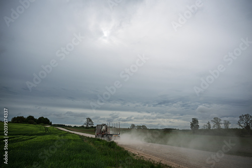 Country dirt road stretching through rural landscapes and green meadows on a cloudy day.