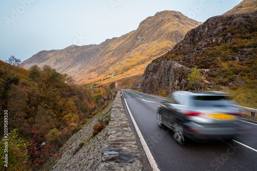 Vehicle travelling through Glencoe, Scotland, along a winding Highland road surrounded by dramatic mountains, autumn colours and rugged landscapes in the Scottish Highlands.