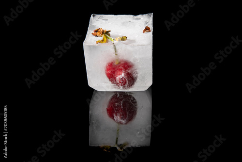 Foto A cherry is trapped in a large ice cube, with reflection on a shiny black backgr