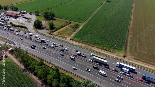 Highway Traffic Jam: An aerial view captures a bustling highway choked with a significant traffic jam, highlighting the congestion amidst agricultural fields under a bright sun.