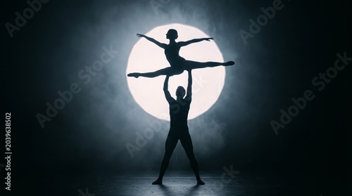 Two dancers appear in silhouette as they perform a ballet lift in front of glowing spotlight. Concept of elegance, performance, and art, ideal for media, advertising, artistic projects. Generative AI.