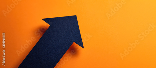 Dark blue paper arrow pointing up on bright orange background in modern design style