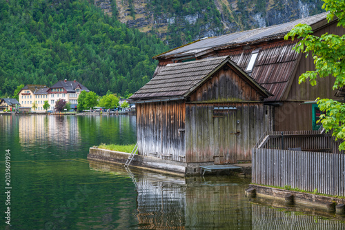 Foto Weathered wooden boathouse beside calm alpine lake, green mountains and village buildings reflected in water, Hallstatt, Austria