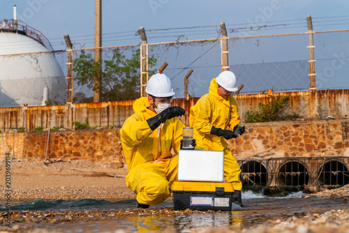 Bild auf Leinwand Two hazmat experts in yellow suits and white hard hats analyze toxic wastewater pollution with a laptop