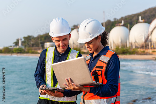 Obraz na plátně Two marine engineers in hard hats and safety vests review a laptop
