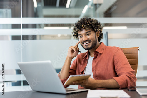 Fotografía Young indian man with curly hair smiling confidently while working on a laptop a