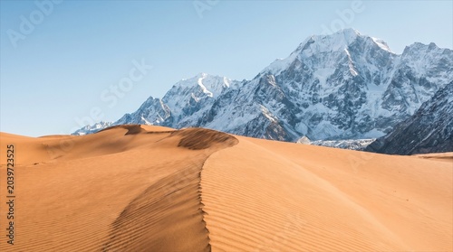 Breathtaking contrast of golden sand dunes and majestic snow-capped mountains under a clear blue sky