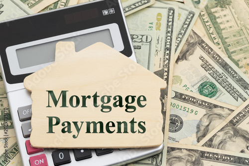 Fotografie Mortgage Payments text on a wood house with calculator on twenty dollar bills fo