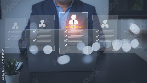 Human Resources Recruitment and Top Candidate Selection Concept. A businessman sits behind a laptop, reviewing virtual candidate profiles floating in the foreground.