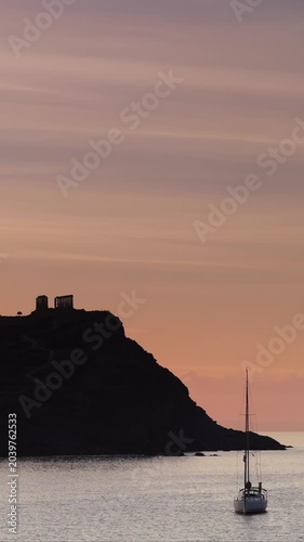 Seascape at dawn with yacht on water and ruins of an ancient temple of Poseidon, Archaeological site in Greece, Cape Sounion. Vertical video, timelapse.