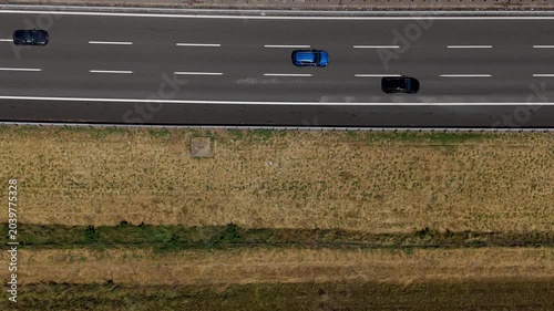 Aerial View of Highway Traffic: A high-angle shot captures the movement of cars on a multi-lane highway cutting through a rural landscape with dry fields. Italy, Milan