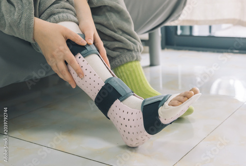Close up of a person adjusting a medical ankle splint on their injured foot indoors.