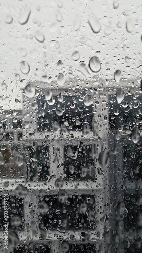 Raindrops on window glass with blurred urban building in background.