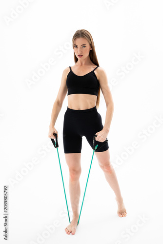 Beautiful girl in sportswear is training with an expander on a white background