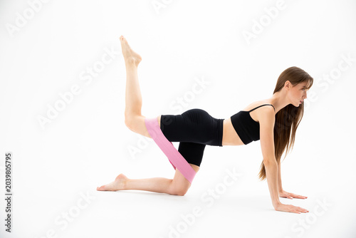 Sporty beautiful girl in sportswear is training with an expander on the floor on a white background