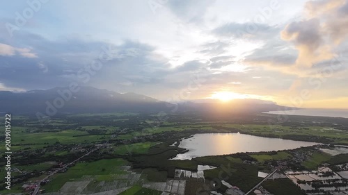 Aerial sunset over lake and mountain valley. Drone view captures a tranquil landscape of lakes, wetlands and farmland  as the setting sun casts warm light across the tropical countryside.