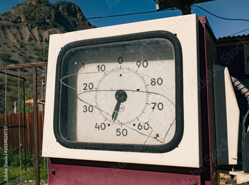 Vintage fuel pump display with broken glass dial on a sunny day in a rustic mountain area