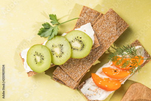 Fresh crunchy rye crispbreads with different toppings on green table, top view