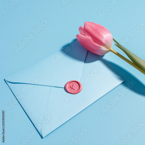 A pink tulip lying on a blue envelope sealed with a pink wax seal, romantic message