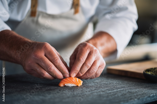 A chef's hands carefully arranging a piece of salmon sushi on a dark surface, culinary art