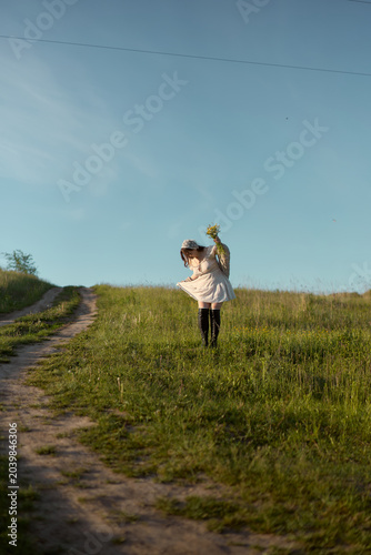 Young girl twirling joyfully in a sunlit meadow on a warm spring day, holding wildflowers in her hand while walking a winding path
