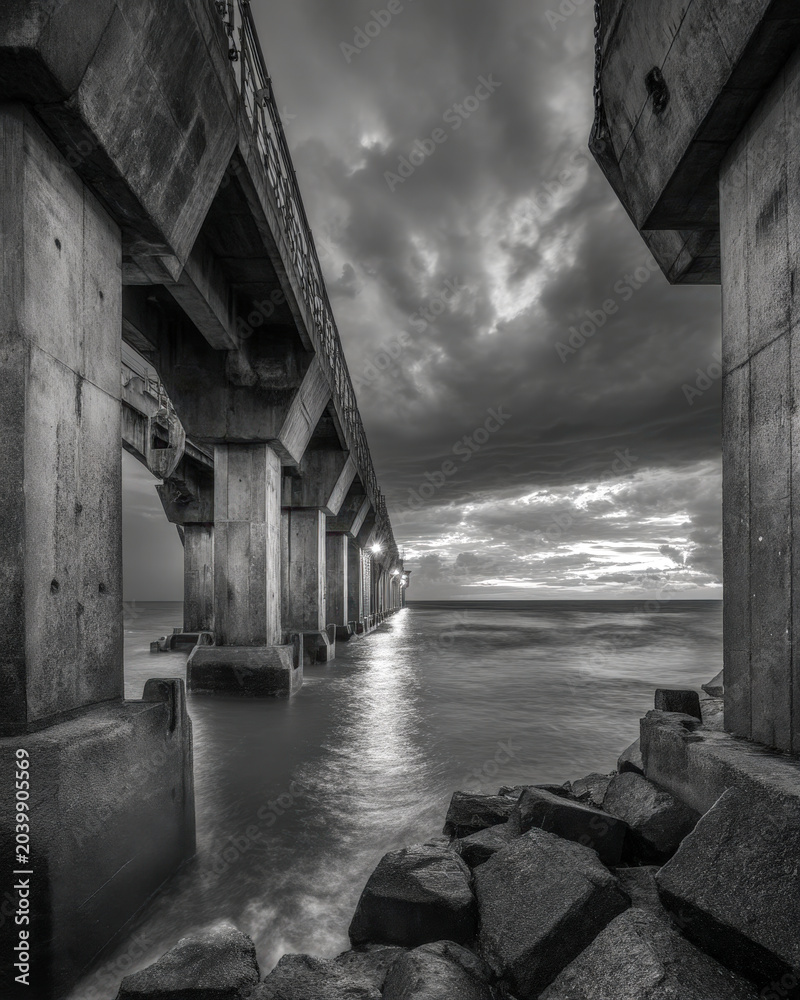 Obraz premium Black and White Concrete Seawall Under Storm Clouds with Rough Water