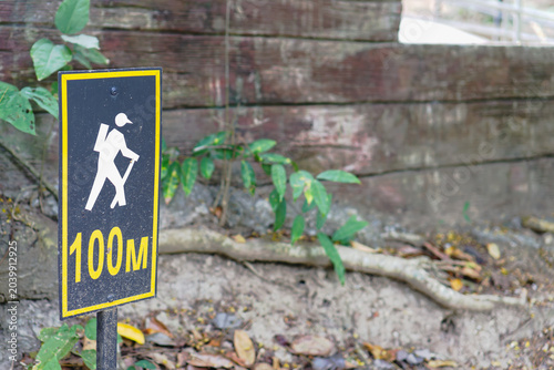 Hiking trail sign with a trekking icon and 100M text in a natural forest park.