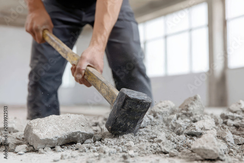 Construction worker using sledgehammer breaking concrete manual labor demolition strength dust indoor renovation safety effort Breaking concrete with sledgehammer construction worker showing