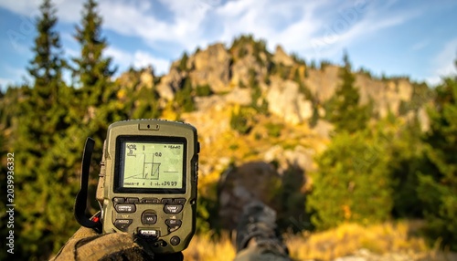 Rugged handheld GPS device displays satellite coordinates and elevation in a mountainous outdoor setting.