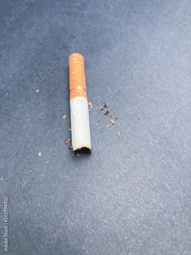 used cigarette butt, ash and tobacco debris on dark surface 